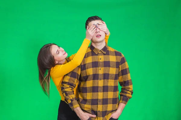 Mulher fechando seus olhos namorado para fazer uma surpresa para ele, ele está em antecipação sobre fundo verde . — Fotografia de Stock