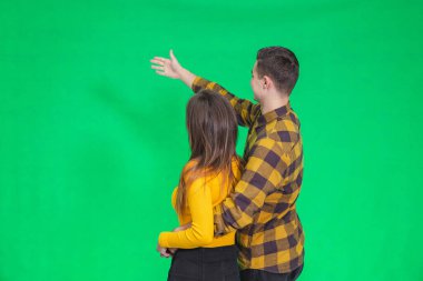 Amazed young people looking and pointing away at something really increadible on green background.