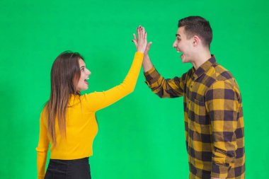 Cheerful young couple giving high five, celebrating their success over green background.