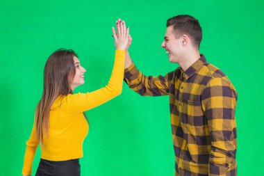 Cheerful young couple giving high five, celebrating their success over green background.