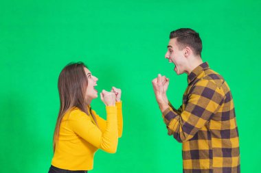 Cheerful young couple clenching their fists, saying yes, celebrating their success over green background.