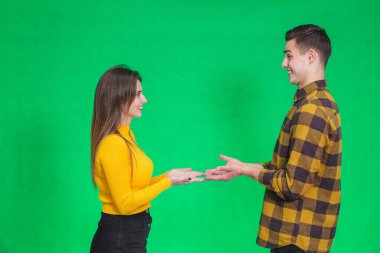 Confused millennial couple isolated on green studio background shrug shoulders feel doubtful and hesitant about something they hold in hands.