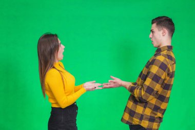 Confused millennial couple isolated on green studio background shrug shoulders feel doubtful and hesitant about something they hold in hands.