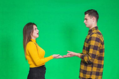 Confused millennial couple isolated on green studio background shrug shoulders feel doubtful and hesitant about something they hold in hands.