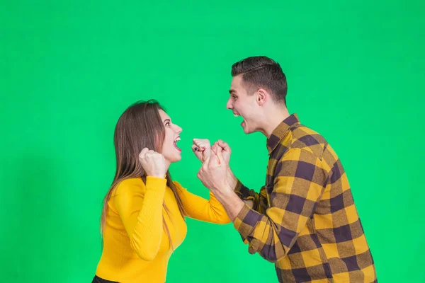 Jovem casal alegre apertando os punhos, dizendo sim, celebrando seu sucesso sobre fundo verde . — Fotografia de Stock