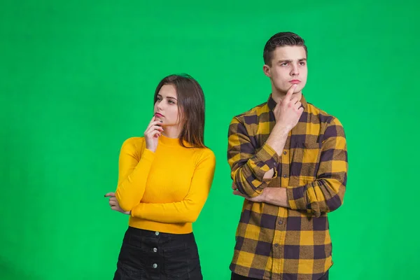 Retrato de um belo jovem casal em pé sobre fundo verde, pensando, mantendo os dedos no queixo . — Fotografia de Stock