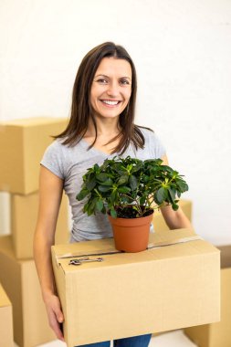 Female carring big carton box packed to be delievered to new house and smiles to the camera with beaming smile. Concept for buying real estate.