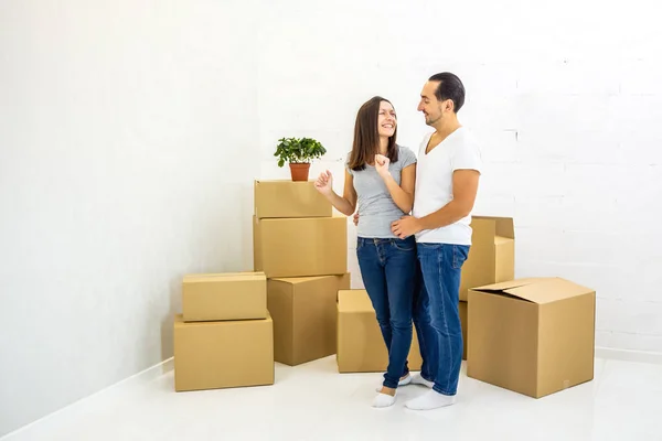 Sorrindo casal de pé juntos, abraçando em seus novos apartamentos com pilhas de caixas no fundo . — Fotografia de Stock