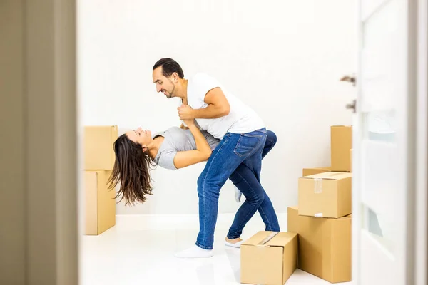 Picture of a cheerful couple dancing after moving into their new apartment with piles of cardboard boxes. Door blurred on the forefront. — Stock Photo, Image