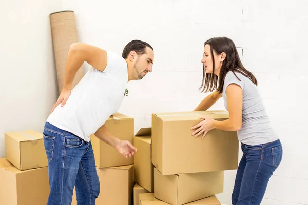 Man suffering from cramp in back while stacking boxes, preparing for relocation, woman tries to help him. — Stock Photo, Image