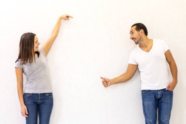 Happy married couple standing side by side holding hands, pointing at the copyspace on white background.