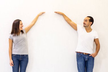 Young couple planning improvements to an apartment standing measuring the height of something against a white wall.