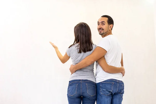 Jeune couple prévoyant des améliorations à un appartement debout mesurant la hauteur de quelque chose contre un mur blanc . — Photo