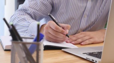 Businessmans hand is writing important down. Close up. Copy space. Blurred forefront. Focus is on background. Crop. 4K.