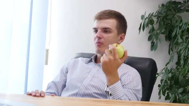 Young businessman is eating apple in the office. Close up. Copy space. 4K. — ストック動画