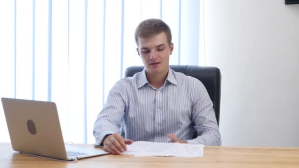 Jovem empresário está lendo papelada na mesa no escritório. Deita-os fora e deita-se na cadeira do escritório. Fecha. Espaço para cópia. 4K . — Vídeo de Stock