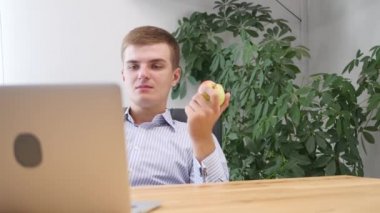 Genç iş adamı ofiste elma yiyor. Bulanık ön cephe. Kapatın. Uzayı kopyala 4k.