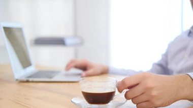 İşadamı dizüstü bilgisayarla çalışıyor ve bulanık arka planda kahvesini yudumluyor. Kapatın. Uzayı kopyala 4k.