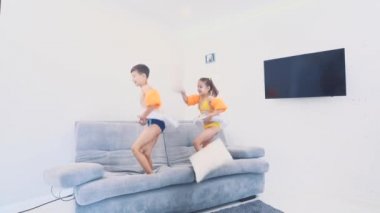 Two little kids, dressed in swimming suits, are happy to go on a trip. They are jumping on the sofa. Copy space. 4K.