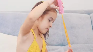 Adorable and little girl with pony-tail blows bubbles. Close up. Copy space. 4K.