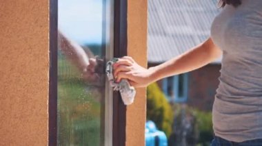Woman is cleaning glass with a grey rag outside. Copy space. Close up. Blurred background. 4K.