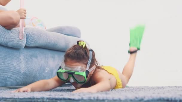 Little girl, wearing swimming suit, flippers and goggles imitating swimming, layinge on the carpet. Copy space. 4K. — Stock Video