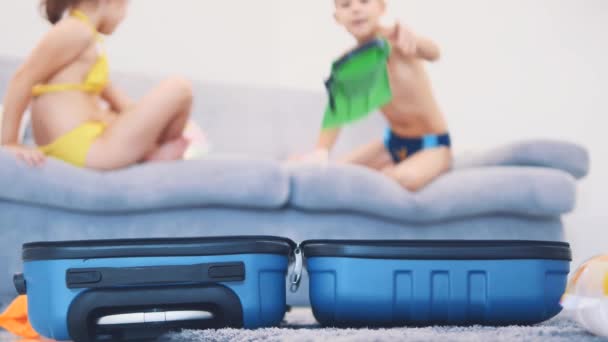 Two little kids, dressed in swimming suits, are happy to go on a trip. They are packing a suitcase. Copy space. 4K. — Stok video