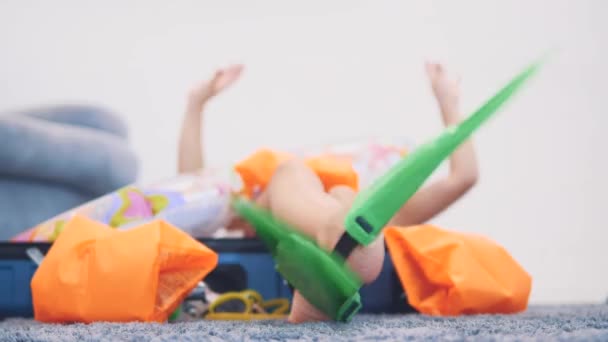 Little girl, wearing swimming suit, flippers and goggles imitating swimming, layinge on the suitcase. Copy space. Close up. 4K. — Stock Video