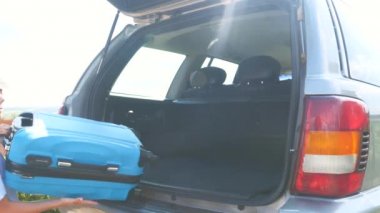 Girl and boy put suitcases into the car boot. Close up. Copy space. 4K.
