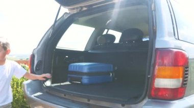 Girl and boy put suitcases into the car boot. Close up. Copy space. 4K.