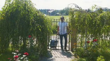 Handsome man opens a gate. He is arriving to vacation with his suitcase. Copy space. 4K.