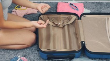 Mom is getting ready to go on weekend with a huge blue suitcase. She counts how many things she should take out. Close up. Getting ready for travel. 4K.