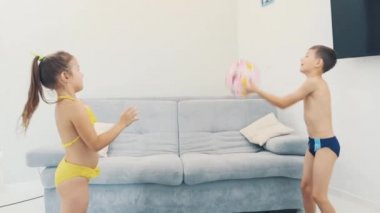 Two little kids, dressed in swimming suits, are happy to go on a trip. They are playing with blown ball. Copy space. 4K.