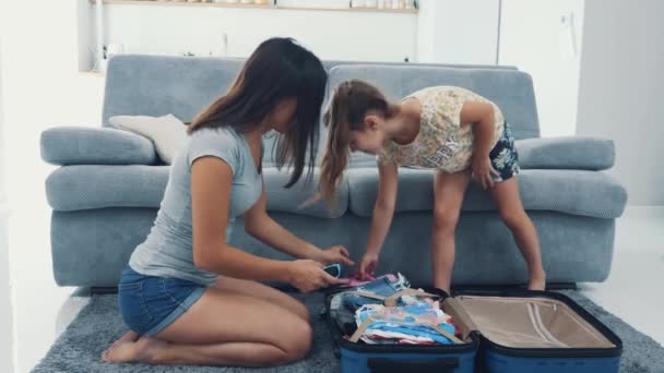 Mamá está haciendo una maleta azul enorme. La niña lleva su ropa para ponerla en la maleta. Preparándose para viajar. 4K . — Vídeos de Stock