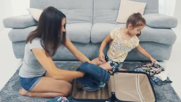 Мама збирає величезну синю валізу. Маленька дівчинка їй допомагає. Готуючись до подорожі. 4k. — стокове відео