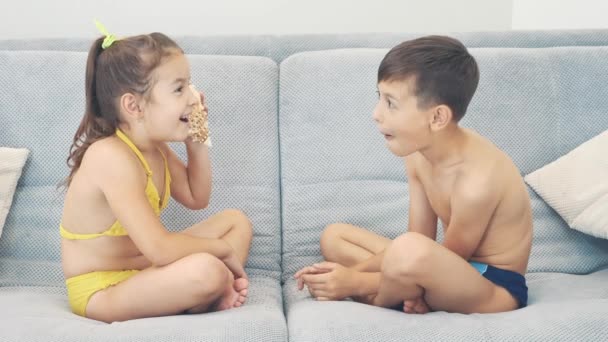 Entzückende kleine Kinder sitzen auf dem Sofa und lauschen einer großen Muschel. Kopierraum. 4k. — Stockvideo