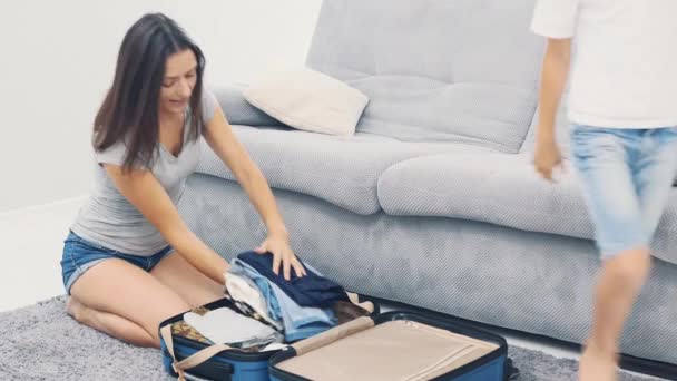 Mamma sta preparando un'enorme valigia blu. Il bambino sta portando i suoi vestiti da mettere in valigia. Mi sto preparando per il viaggio. 4K . — Video Stock
