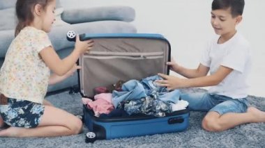 Küçük şirin çocuklar evde bir bavulu kapatmaya çalışıyorlar. Üzerinde oturuyorlar. Yakın çekim 4k.