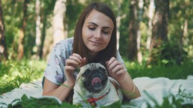 Smiling lady is taking free time with her dog. Woman relaxing in the nature with her little pug dog. Close up. Copy space. 4K.