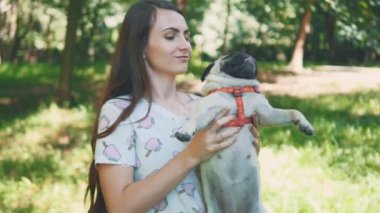 Young woman is swinging and swaying her pug dog on the park packground. Copy space. 4K.