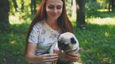 Young woman feeding her small pug dog with sweet ice-cream. Close up. Crop. Copy space. 4K.