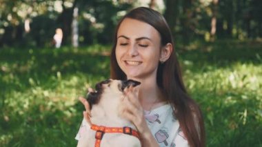 Smiling lady is taking free time with her dog. Woman relaxing in the nature with her little pug dog. Crop. Close up. Copy space. 4K.