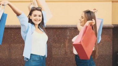 Two happy girls with shopping bags are boasting with purchses and showing them. Close up. Copy space. 4K.