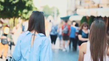 Two beautiful girls have fun walking down the street with their purchases after shopping. Back view. Close up. Copy space. 4K.