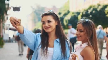 Smiling teenage girls are taking selfie by smartphone, being on summer city park background. Copy space. Close up. 4K.