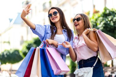 Inspired women are using smartphone vlogging their shopping day on blurred city background.
