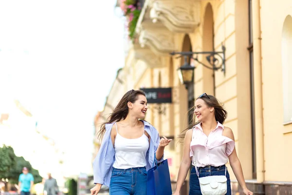 Two beautiful girls on shopping together in the city center, with a lot of bags with purchases in hands. — Stockfoto
