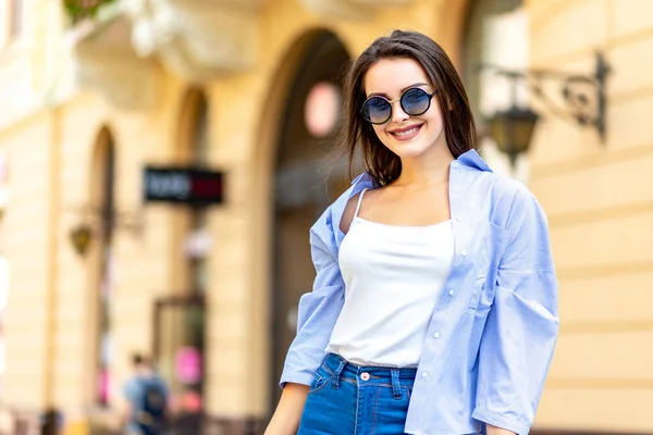 Wanita hipster yang menarik dengan kacamata hitam bergaya berjalan-jalan di pusat kota dalam cuaca cerah . — Stok Foto
