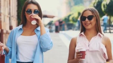 Two attractive young women are walking and talking in a summer street with coffee cups. Close up. Copy space. 4K