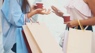 Two attractive young women are walking and talking in a summer street with coffee cups. Close up shopping bags. Crop. Copy space. 4K